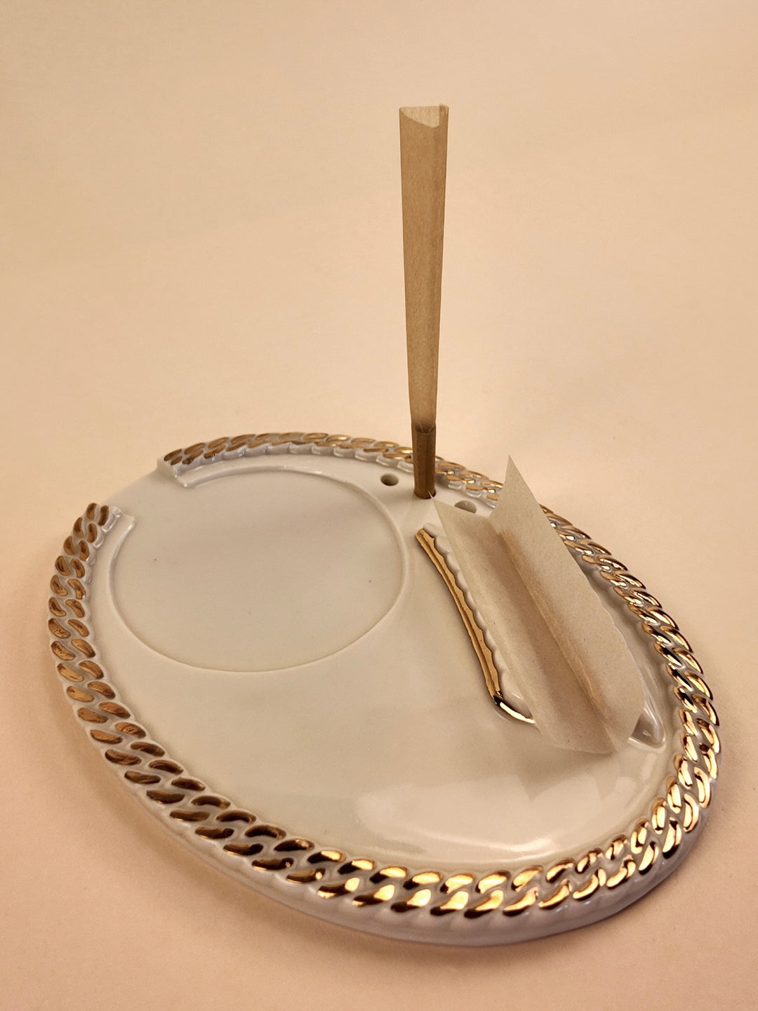 A white porcelain ashtray with a silver-toned metallic chain-link border and two silver decorative accents, shown on a solid beige background.