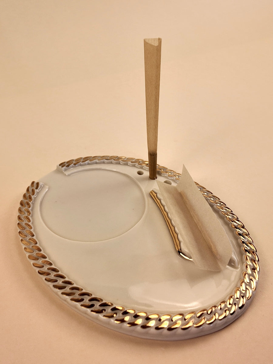 A white porcelain ashtray with a silver-toned metallic chain-link border and two silver decorative accents, shown on a solid beige background.