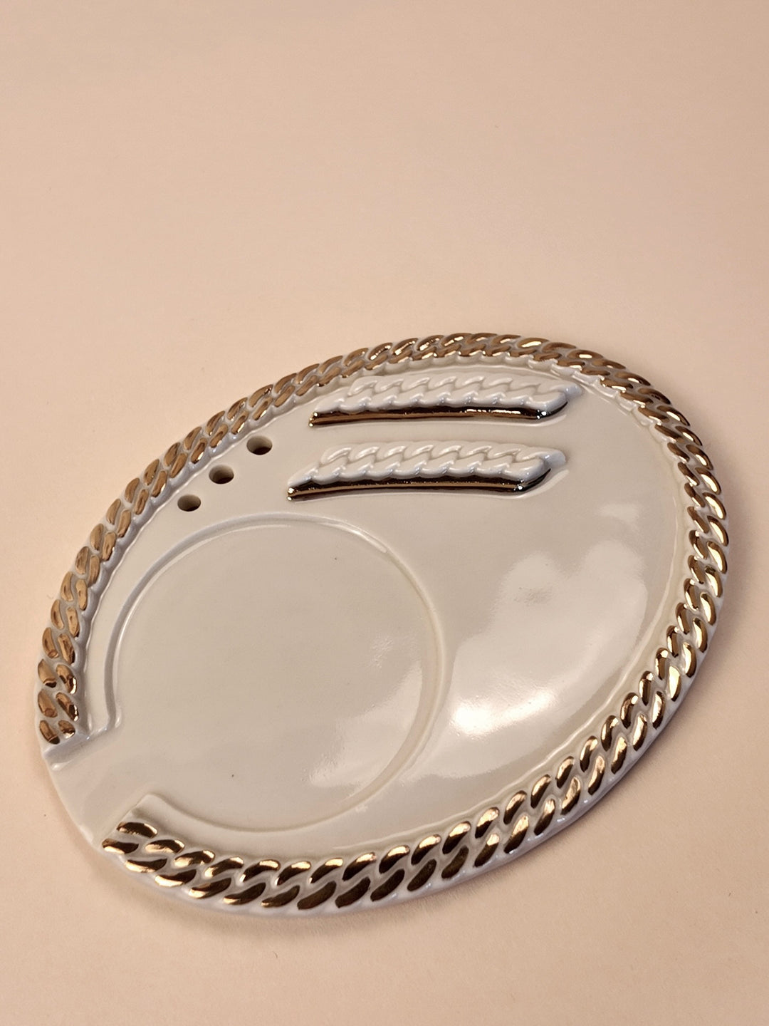 A white porcelain ashtray with a silver-toned metallic chain-link border and two silver decorative accents, shown on a solid beige background.