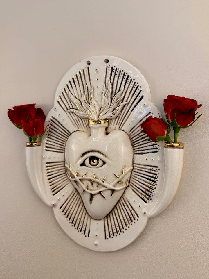 A decorative porcelain wall plaque featuring a stylized white heart with an eye and thorn details, mounted on a beige wall with reference Red Roses