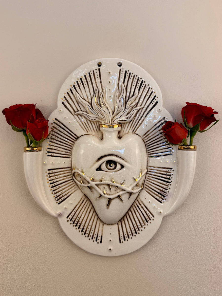 A decorative porcelain wall plaque featuring a stylized white heart with an eye and thorn details, mounted on a beige wall with reference Red Roses